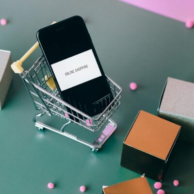 Conceptual image of online shopping with a smartphone in a miniature cart.
