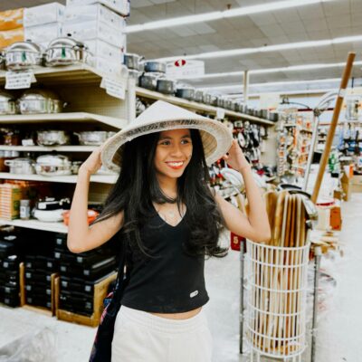 Smiling woman wearing a conical hat in a Dallas supermarket, enjoying shopping.